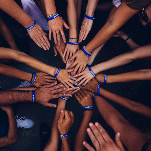 Group of people putting their hands in together standing in a circle wearing wrist blue bands